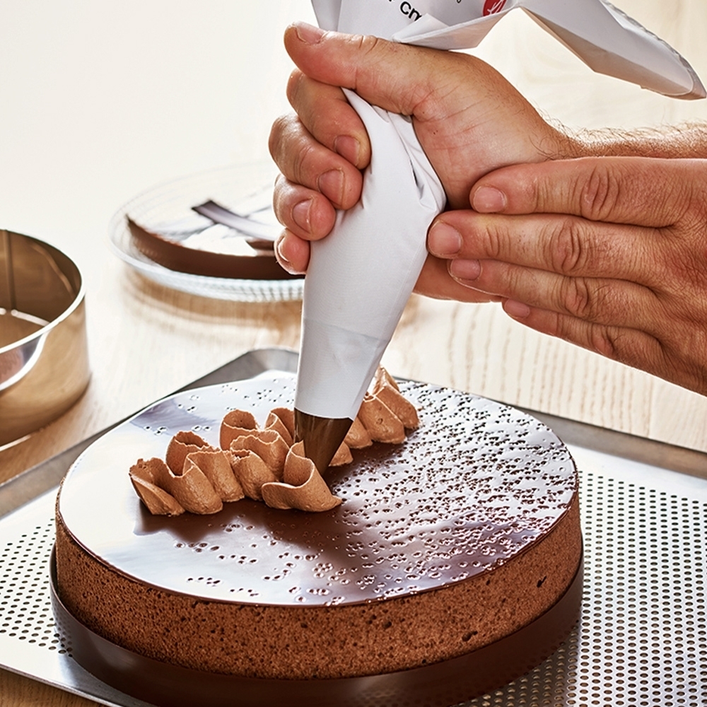 Hand decorates chocolate cake with piping bag
