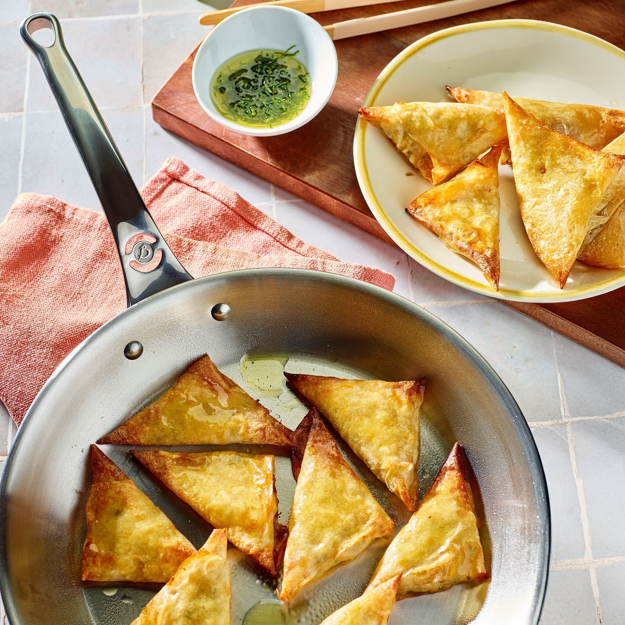 Golden fried pastry triangles in pan with dip